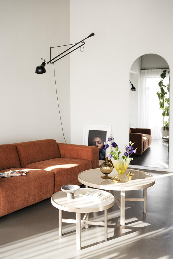 Ljust vardagsrum med orange soffa, vita runda soffbord, svart vägglampa och spegel