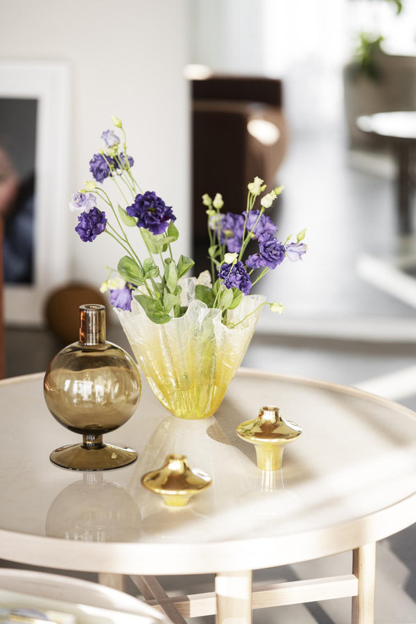 Gul glasvas med lila blommor och parfymflaskor på vitt bord i modern inredning