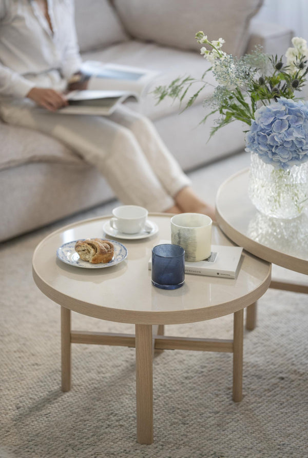 Runt soffbord i ljust trä med kaffe, bakverk och blå dricksglas i skandinavisk vardagsrumsmiljö