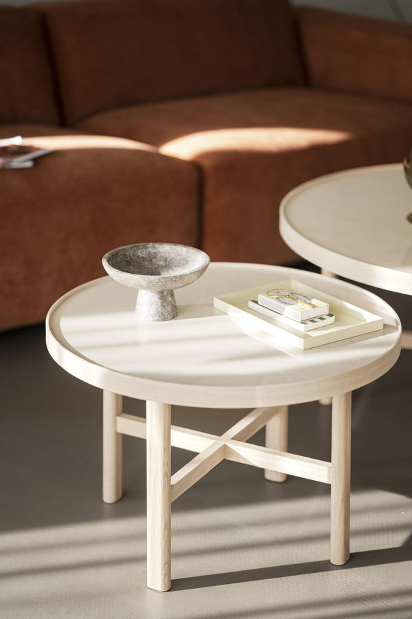 Runt soffbord i ljust trä med bricka och dekoration framför brun soffa