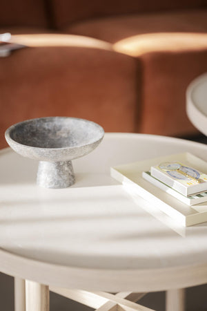 Grå marmor skål på fot placerad på vitt sidobord med böcker i vardagsrumsmiljö