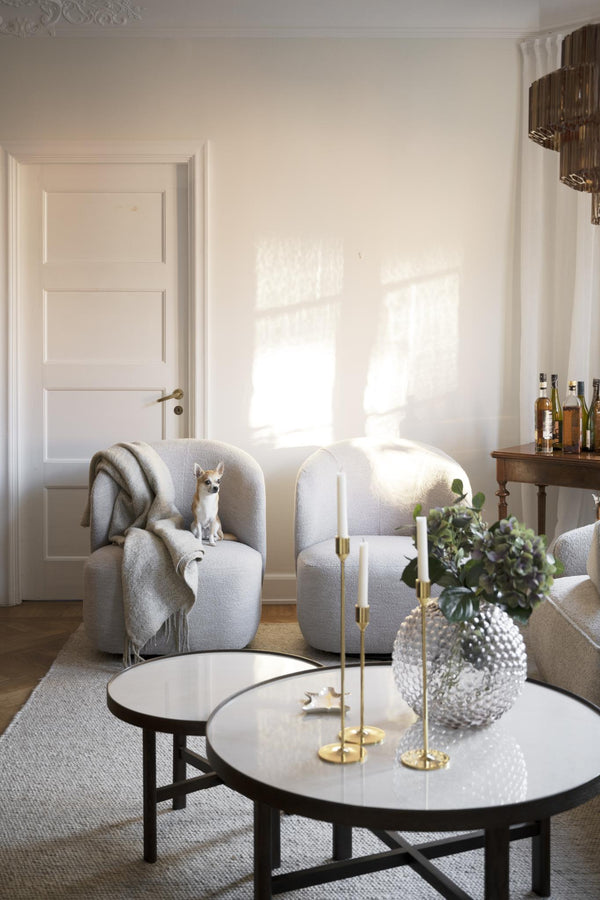 Ljust vardagsrum med två beiga fåtöljer, runda soffbord i glas och marmor, samt elegant belysning