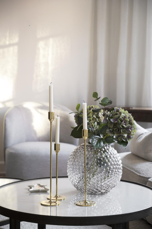 Ljusstakar i mässing med vita ljus och glasvas med hortensia på soffbord i vardagsrum