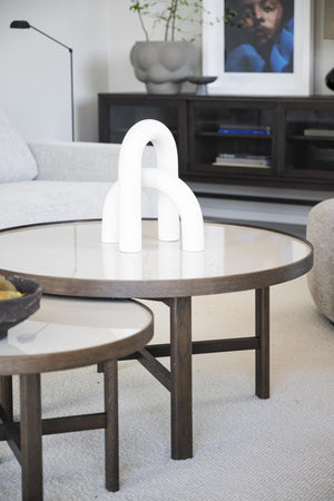 Vit skulpturell vas i bågform på runt soffbord i modern skandinavisk vardagsrumsinredning