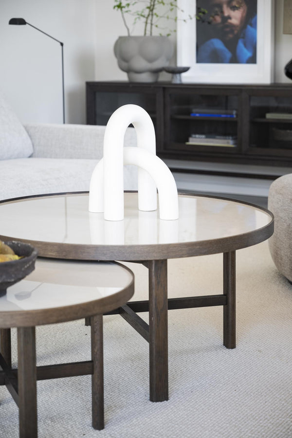 Vit skulpturell vas i bågform på runt soffbord i modern skandinavisk vardagsrumsinredning