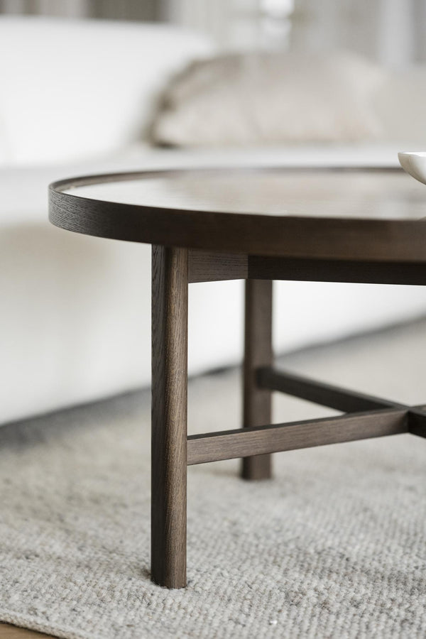 Soffbord i mörk ek med rund bordsskiva och smala ben på ljus matta i skandinavisk stil