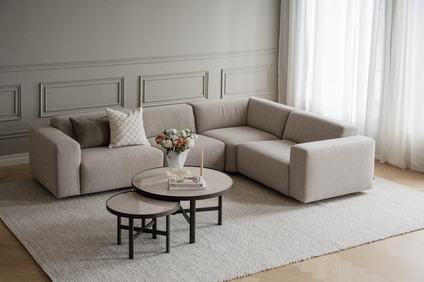 Beige modulsoffa i hörnutförande med runda soffbord och ljus matta i elegant vardagsrum