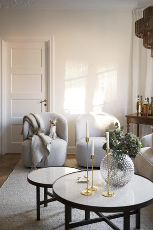 Ljust vardagsrum med två grå fåtöljer, runda soffbord i glas och marmor, samt elegant inredning med hund
