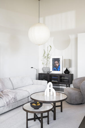 Modernt vardagsrum med vit klotlampa, ljusgrå soffa, runda soffbord och svart skänk mot vit vägg