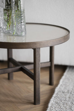 Runt soffbord i trä med ljus stenfärgad yta och smala ben, dekorerat med glasvas med gröna kvistar