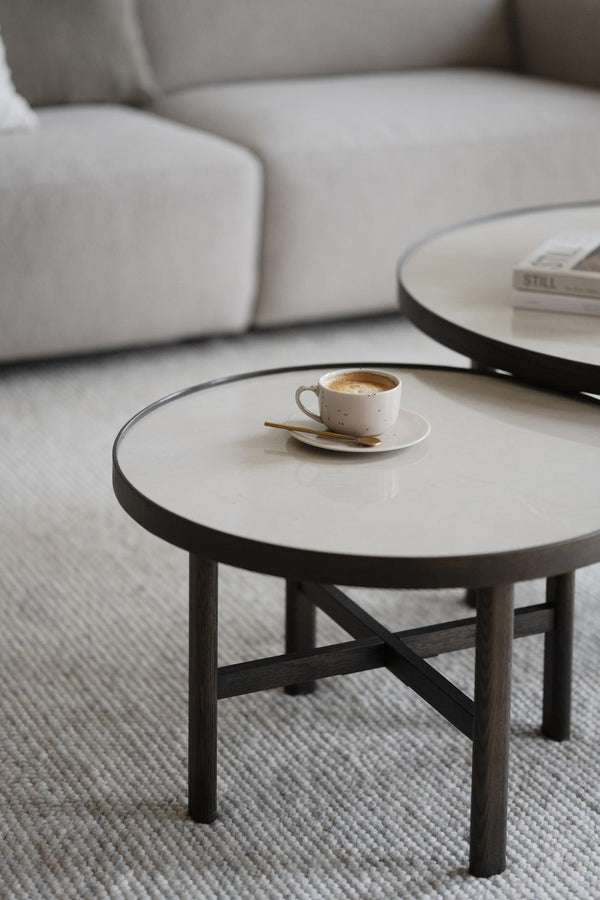 Runt soffbord med vit marmorskiva och svarta träben, kaffekopp med fat på bordet i moderna vardagsrum