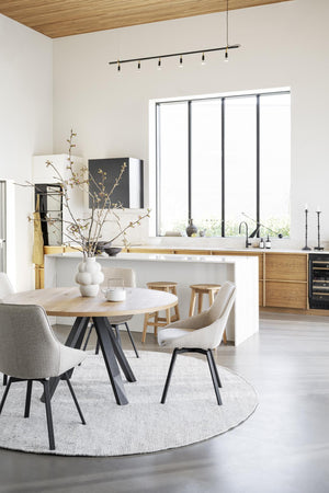 Ljus matplats med runt matbord i trä, beige stolar och öppet kök med trädetaljer och vita väggar