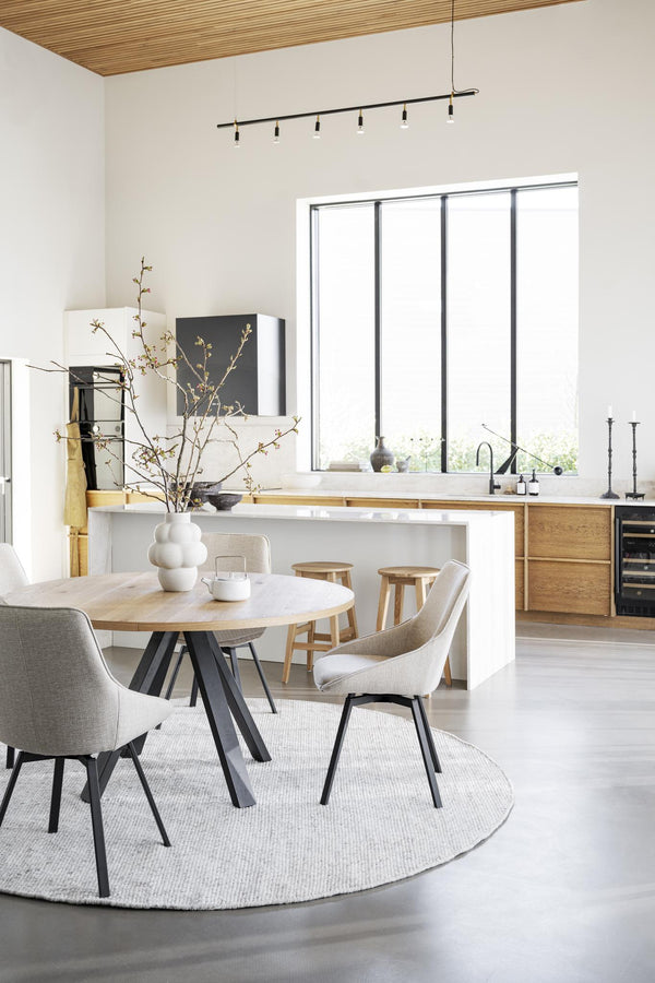 Ljus matplats med runt matbord i trä, beige stolar och öppet kök med trädetaljer och vita väggar