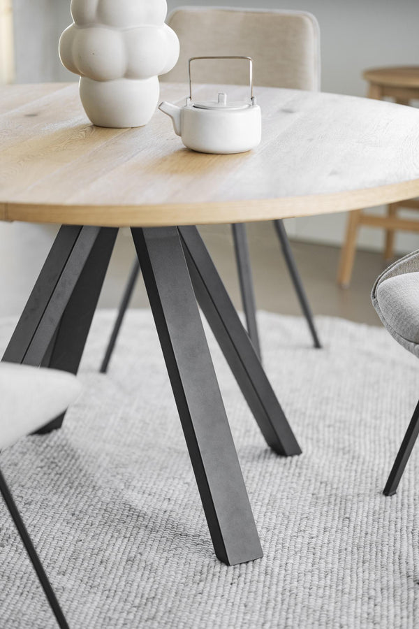 Runt matbord med ljus ekfanér och svarta metallben på grå matta i modern skandinavisk stil