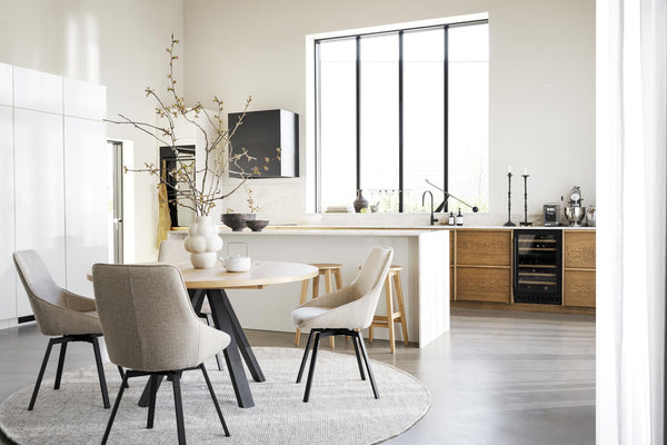 Ljust kök med matplats, runt matbord, beiga stolar och träskåp med vita bänkskivor