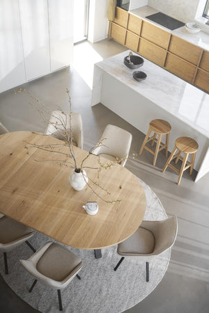 Minimalistiskt kök med matbord i ljust trä, beige stolar och barstolar vid köksö med marmorbänkskiva