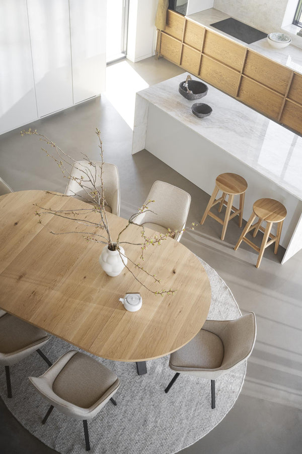 Minimalistiskt kök med matbord i ljust trä, beige stolar och barstolar vid köksö med marmorbänkskiva