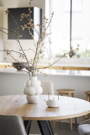 Vit skulptural vas med grenar på runt matbord i ljus skandinavisk matsal
