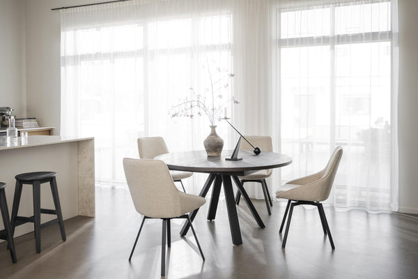 Runt matbord i grått med fyra beige stolar i modern matsal med stora fönster och ljust golv