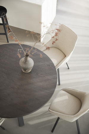 Rund matbord i mörkt trä med beige stoppade stolar och torkad blomsterarrangemang i rustik vas