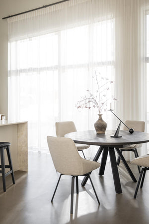 Rund matbord i mörk ek med beige stoppade stolar i modern matsal med vita gardiner och naturligt ljus