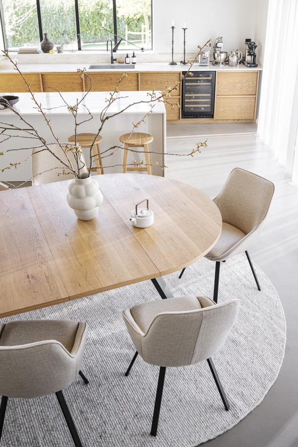 Runt matbord i ljust trä med beige stoppade stolar i modern skandinavisk matsal med öppet kök