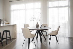 Rund matbord med fyra beige stolar i modern matsal med stora fönster och ljust trägolv