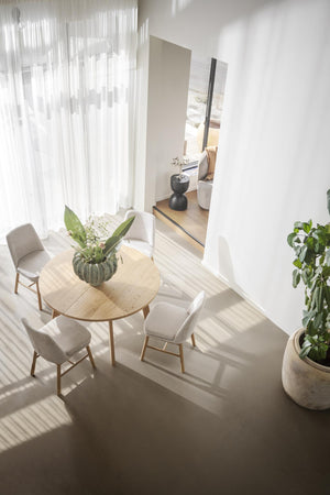 Ljust matrum med runt träbord, beige stolar och vita gardiner i minimalistisk skandinavisk stil