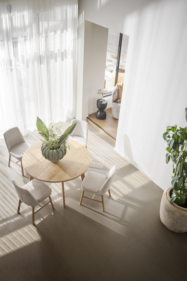 Ljust matrum med runt träbord, beige stolar och vita gardiner i minimalistisk skandinavisk stil
