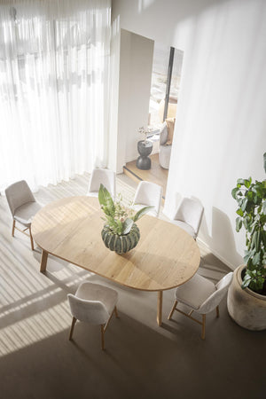 Oval matbord i ljust trä med sex beige stolar i minimalistisk matsal med naturligt ljus