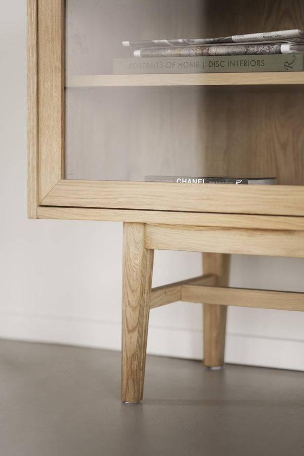 Sängbord i ljus ek med öppen hylla, designade ben och böcker på hyllplanet