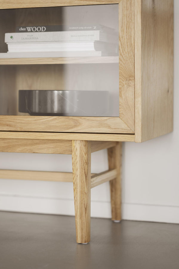 Tv-bänk i ljust trä med öppen förvaring, synliga snickardetaljer och avsmalnande träben med mässingsdetaljer