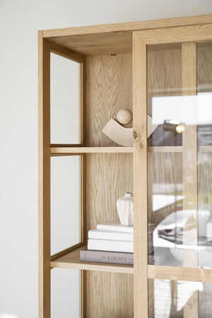 Ljus ekskåp med öppna hyllplan, dekorerad med böcker och keramikvas, glasdörrar med spröjs