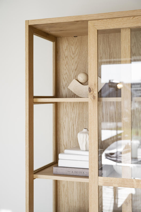 Ljus ekskåp med öppna hyllplan, dekorerad med böcker och keramikvas, glasdörrar med spröjs