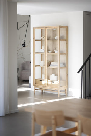 Vitrinskåp i ljust trä med glashyllor och vita dekorationer i minimalistisk skandinavisk stil
