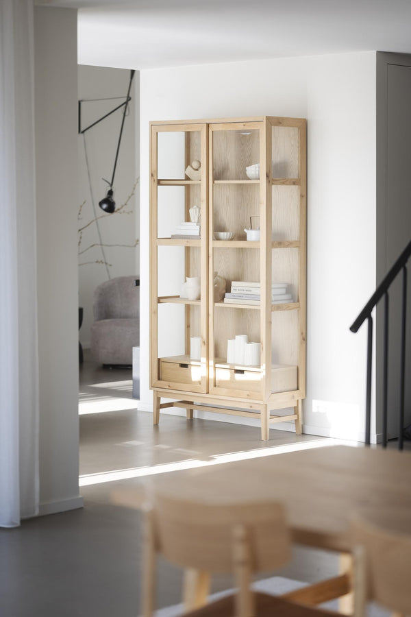 Vitrinskåp i ljust trä med glashyllor och vita dekorationer i minimalistisk skandinavisk stil