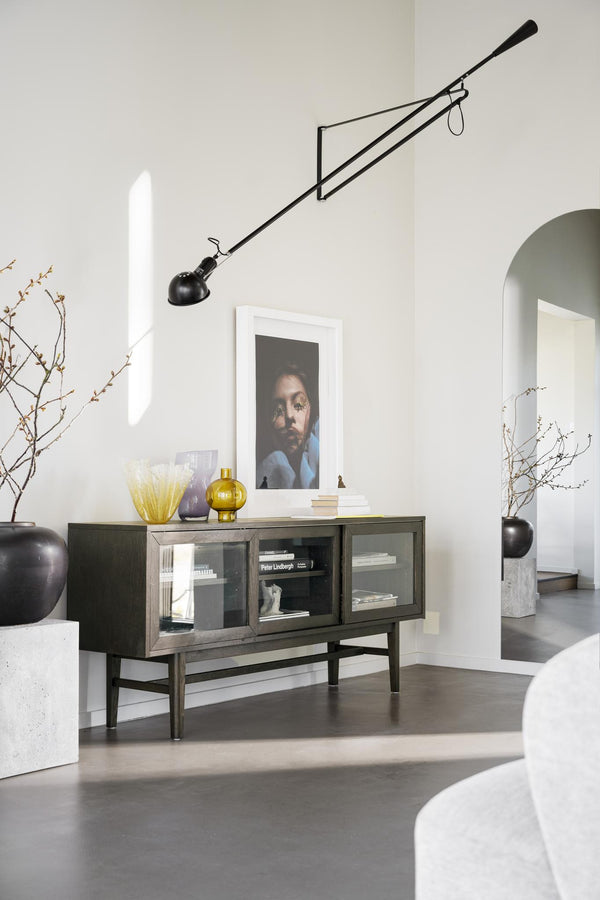 Skänk med glasdörrar i mörkt trä med dekorativa vaser och konst i ljust vardagsrum med designlampa