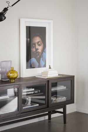 Mörkt TV-bänk i trä med glasprylar, böcker och inramad konst på väggen i modernt vardagsrum