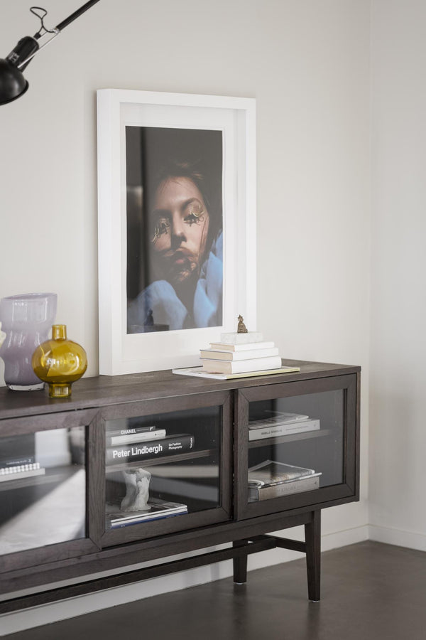 Mörkt TV-bänk i trä med glasprylar, böcker och inramad konst på väggen i modernt vardagsrum