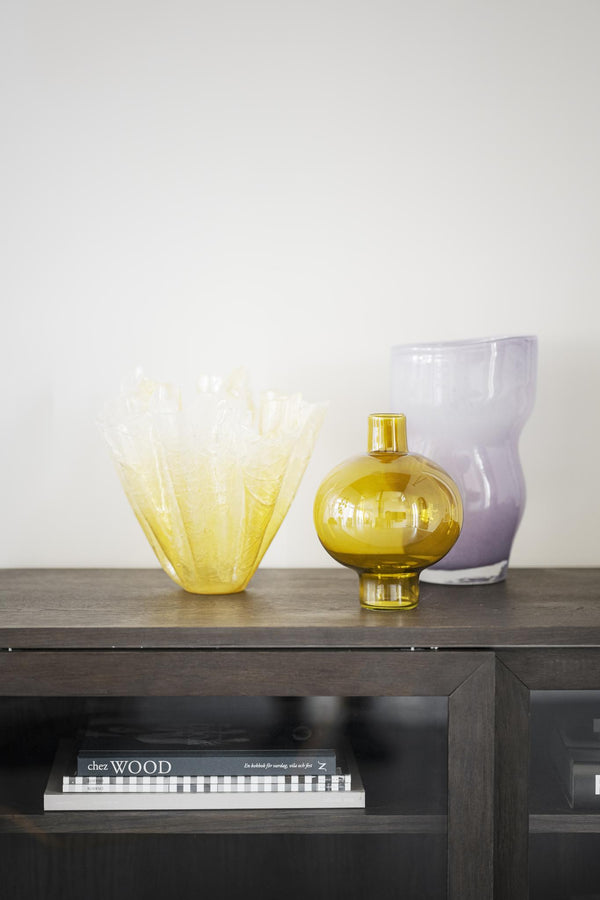 Glasvaser i gult och lila på mörkbrun TV-bänk med böcker