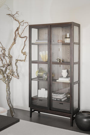 Vitrinskåp i mörkbrun ek med glasdörrar och hyllor, inrett med böcker, vaser och dekorativa föremål