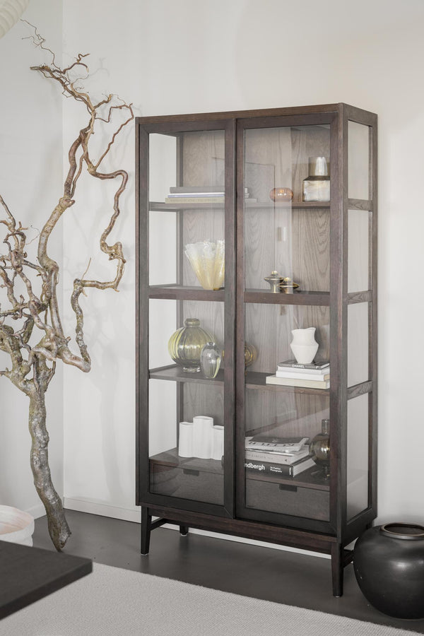 Vitrinskåp i mörkbrun ek med glasdörrar och hyllor, inrett med böcker, vaser och dekorativa föremål
