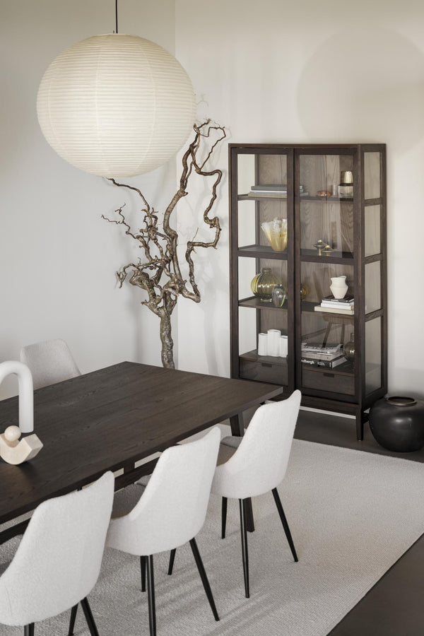 Modern matplats med mörkt träbord, vita stolar, rund rislampa och vitrinskåp med glasdörrar