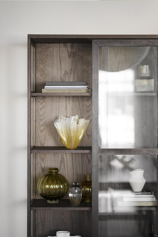 Bokhylla i mörkt trä med dekorativa vaser, böcker och glasföremål i gult och grönt