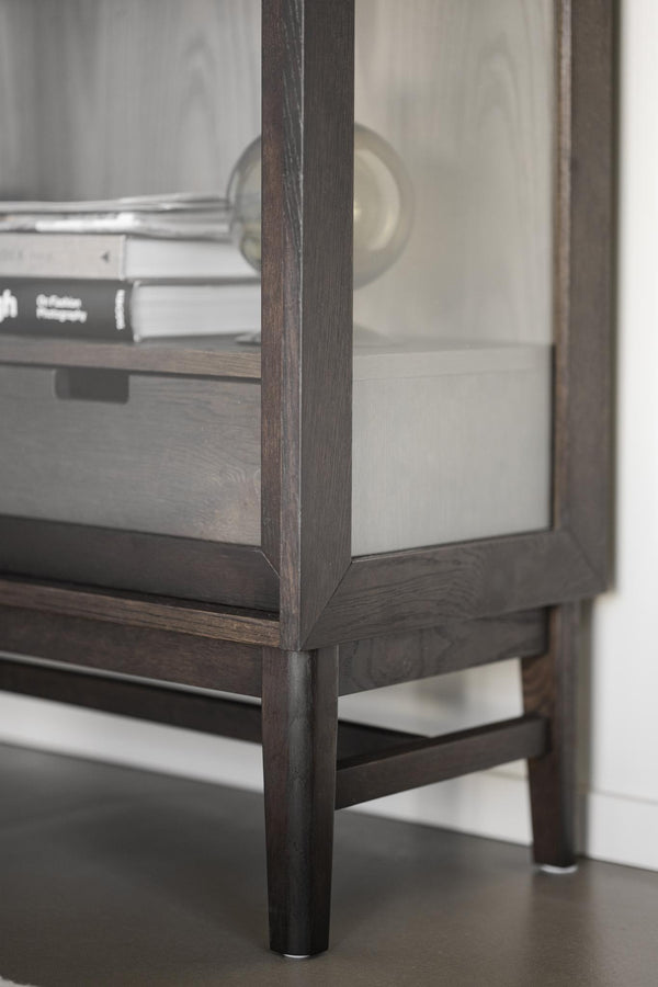 Närbild på möbelben och hörn av vitrinskåp i mörkt trä med glasdörr och synlig bokhylla