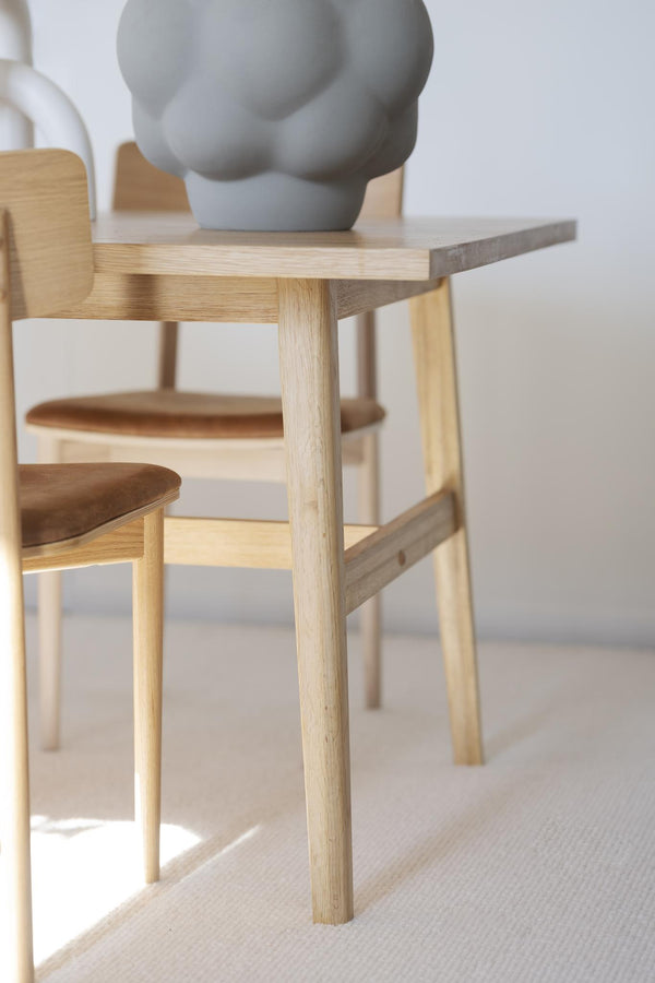 Närbild på ljusa träbord och stolar i skandinavisk design med grå dekorationsvas