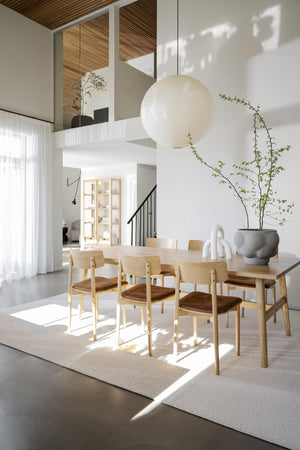 Ljus matsal med träbord, stolar i ljust trä och vit klotlampa i högt i tak med loft