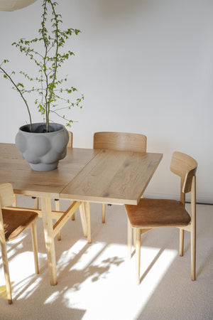 Matbord i ljust trä med matchande stolar och grå krukväxt i minimalistisk skandinavisk matsal