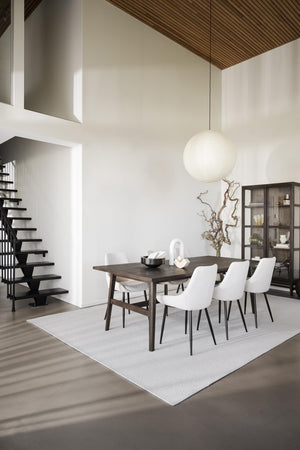 Modern matplats med vit matta, mörkt matbord, vita stolar och spherisk taklampa i minimalistiskt hem