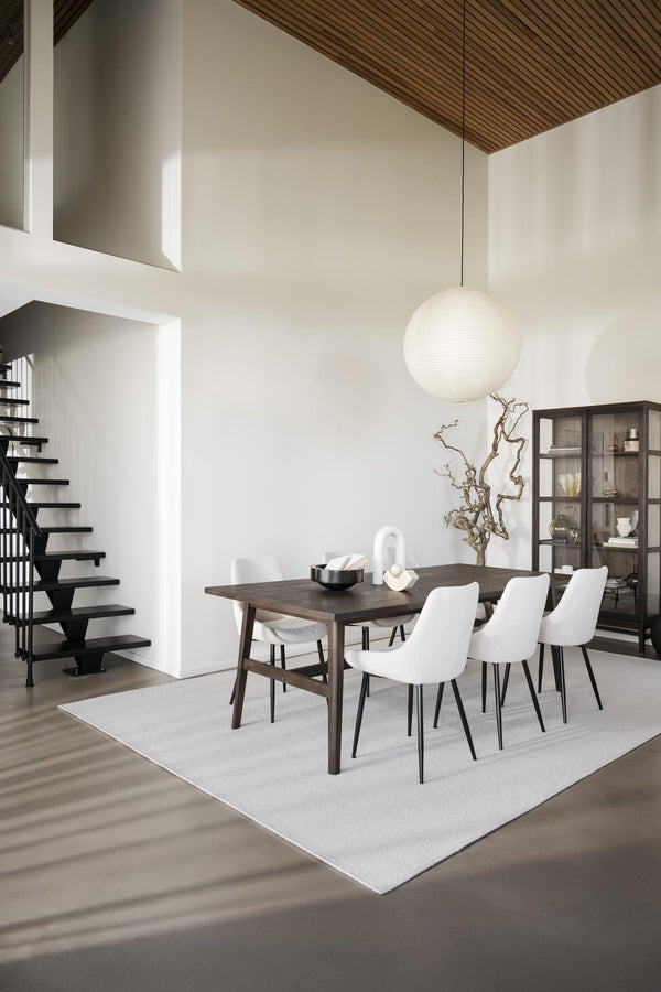 Modern matplats med vit matta, mörkt matbord, vita stolar och spherisk taklampa i minimalistiskt hem